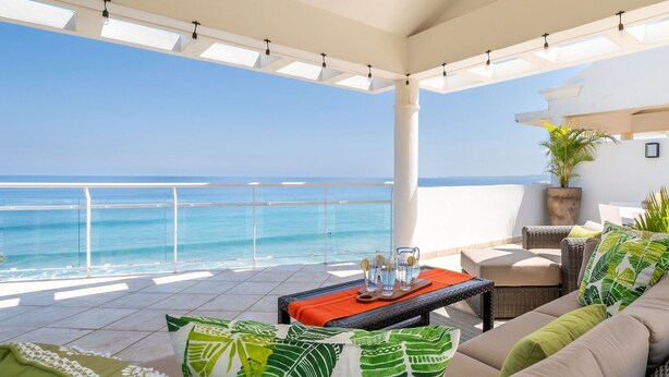 Un balcón con vista al océano, amueblado con un sofá, una mesa y cojines decorativos.