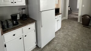 A kitchen with white cabinets, a refrigerator, a coffee maker, and a trash can.