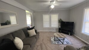 A living room with a gray couch, a coffee table, a TV stand, and a ceiling fan.