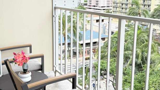 Un balcón con una mesa y una silla, una planta en maceta y vistas de un paisaje urbano con edificios y palmeras.