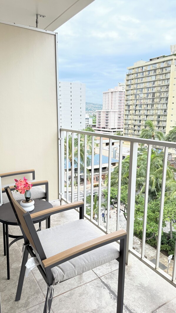 A balcony with a table and chair, a potted plant, and a view of a cityscape with buildings and palm trees.