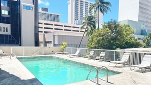 Una piscina en la azotea con agua azul cristalina, rodeada de sillas de descanso y una barandilla blanca.