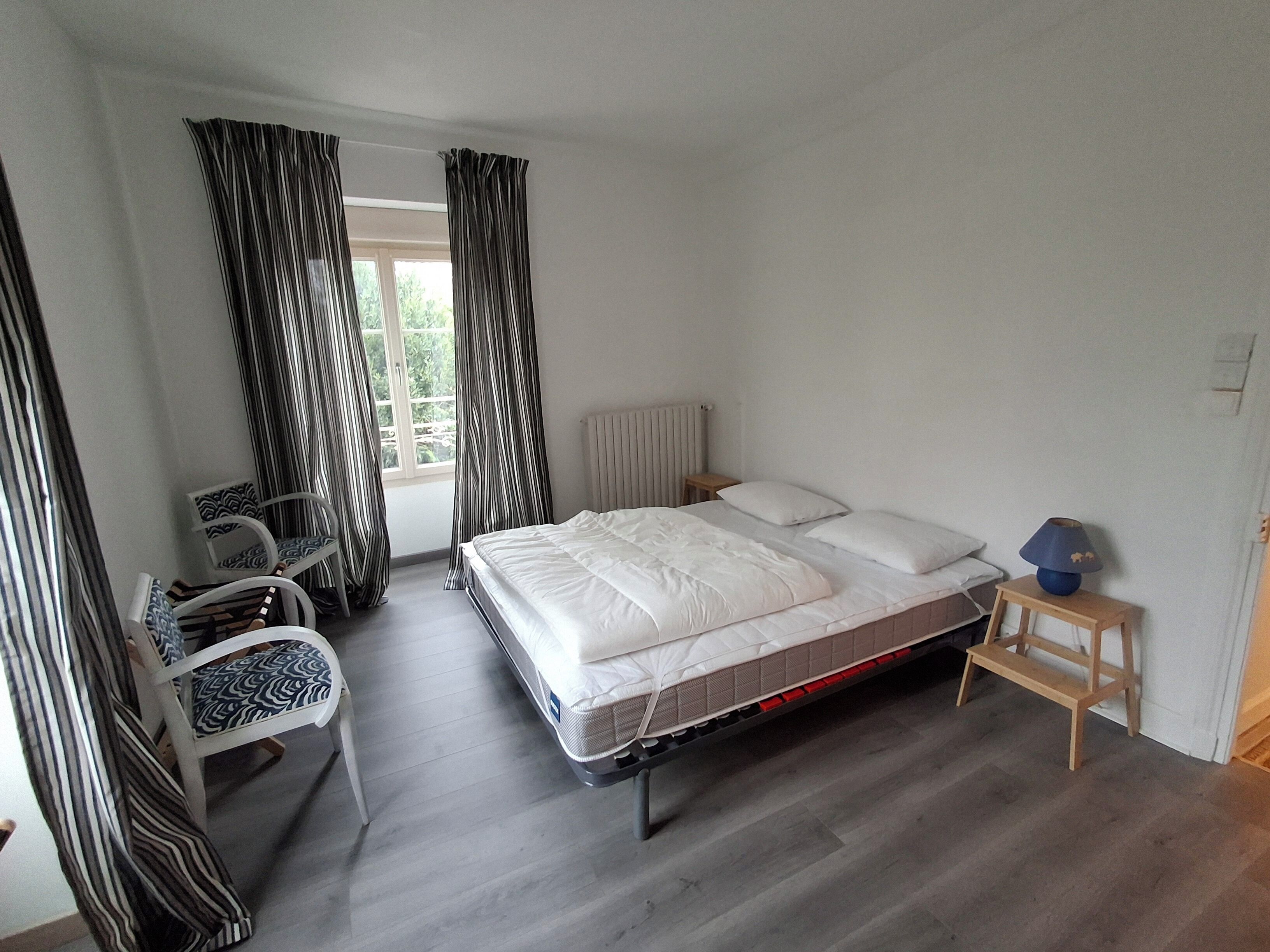 A bedroom with a bed, a chair, a small table, and a window with curtains.