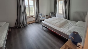 Une chambre à coucher avec un grand lit, un petit bureau, deux chaises et une fenêtre avec des rideaux.