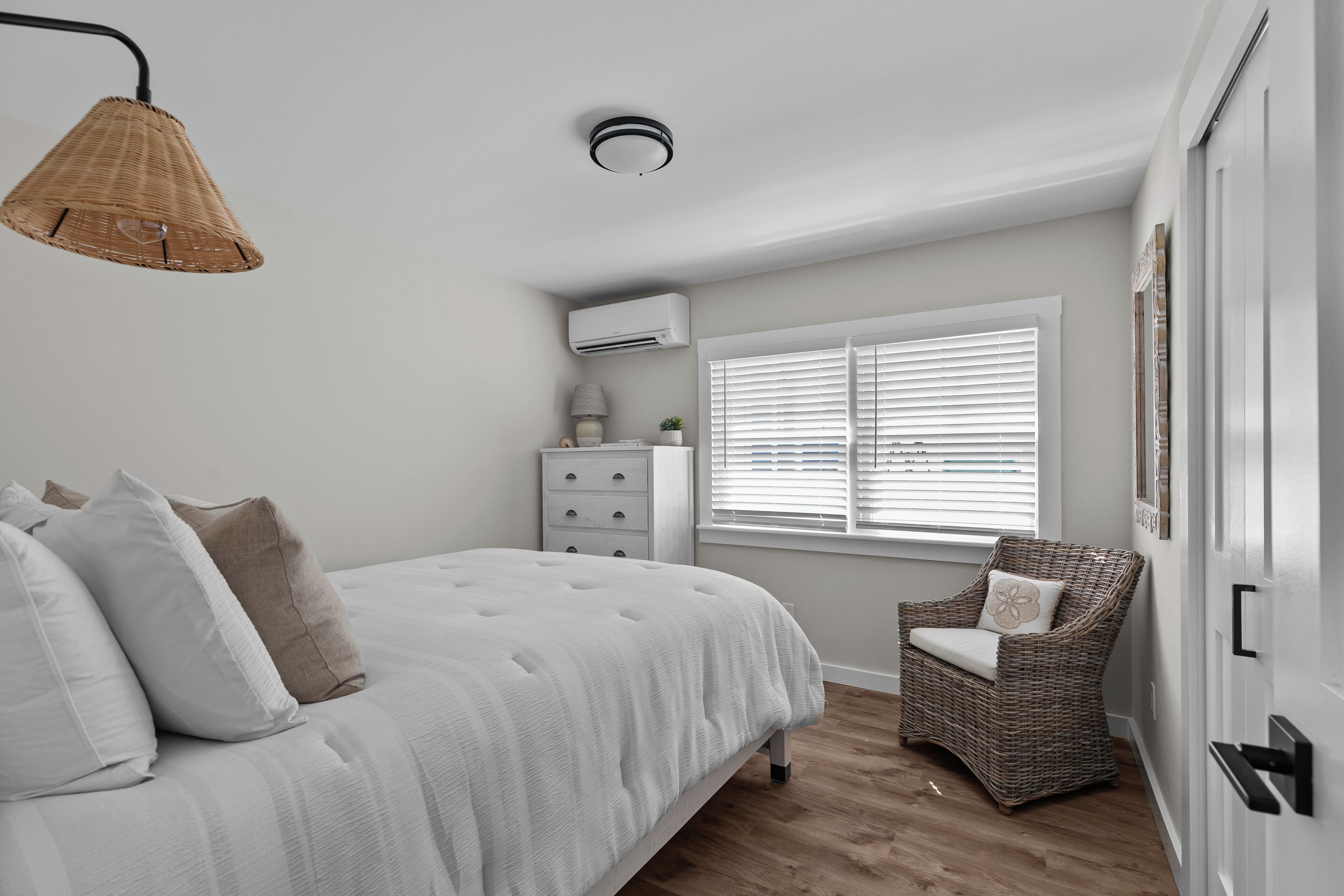 A bedroom with a bed, a chair, a dresser, and a window with blinds.
