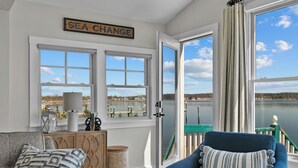 A room with a view of a lake, a blue chair, a wooden cabinet, and a sign that reads "SEA CHANGE".