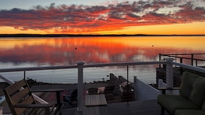A deck with outdoor seating overlooking a calm body of water during sunset.