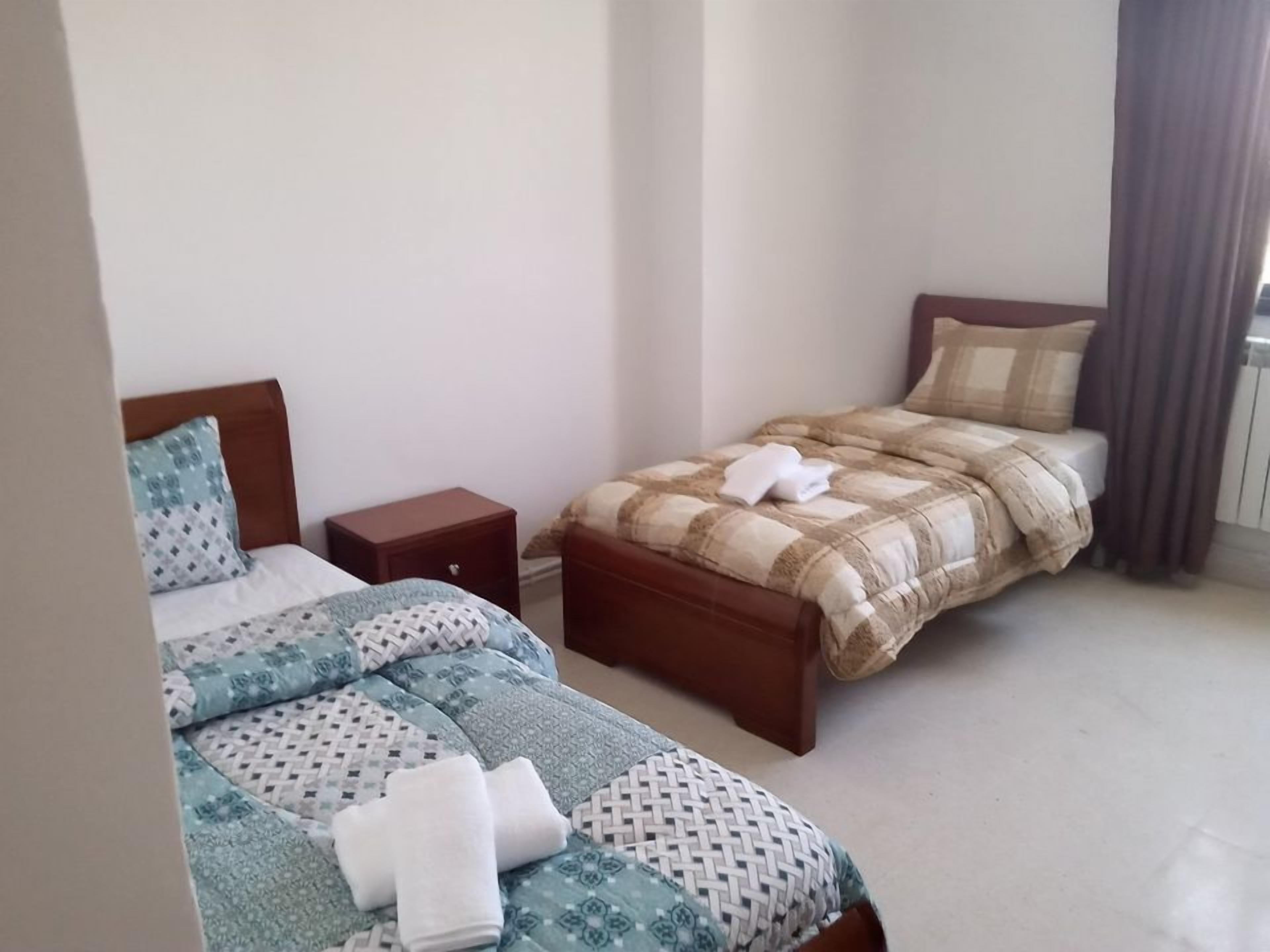 Ein Schlafzimmer mit zwei Betten, jedes mit einer anderen Bettdecke, einem Holznachttisch und einem Fenster mit Vorhängen.