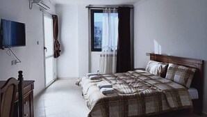 Un dormitorio con cama, televisor montado en la pared, ventana con cortinas y puerta.