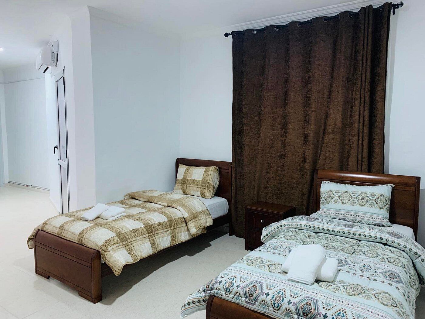 A bedroom with two beds, a wardrobe, and a curtain.