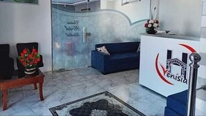 Zona de recepción con un sofá azul, un banco de madera, un separador de vidrio y un logotipo en la pared.