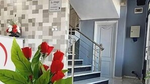 Un área de recepción con pared de azulejos, una planta en maceta con flores rojas y una escalera de fondo.