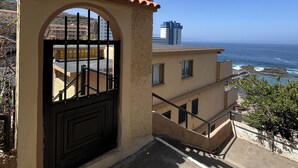 A gated entrance with a tiled roof, a staircase leading to a building, and a view of the ocean and a distant cityscape. - Flat Tarajal SeaView in Mesa del Mar, Tacoronte Tenerife (CN)
