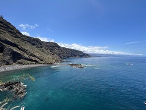 A coastal landscape with rocky cliffs, clear blue waters, and a beach with umbrellas. - Flat Tarajal SeaView in Mesa del Mar, Tacoronte Tenerife (CN)