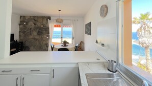 A kitchen with a stone wall, a view of the sea, and a window with a view of palm trees. - Flat Tarajal SeaView in Mesa del Mar, Tacoronte Tenerife (CN)