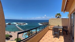 A balcony with a view of the ocean, a pool, and a table with chairs. - Flat Tarajal SeaView in Mesa del Mar, Tacoronte Tenerife (CN)