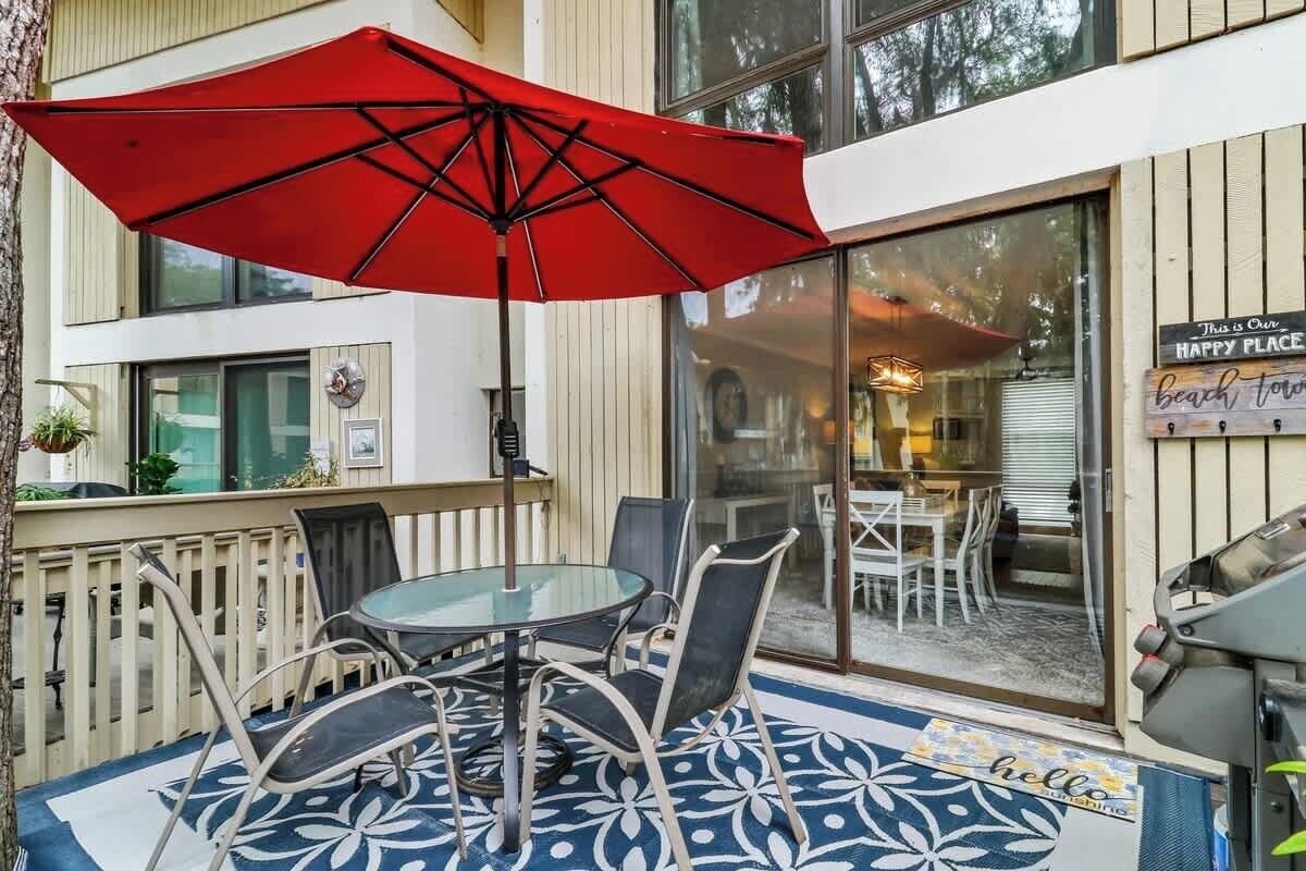 A patio with a glass table and chairs, a red umbrella, and a sign reading "This is our happy place."