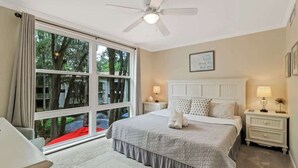 A bedroom with a large window, a ceiling fan, a bed with white bedding, two bedside tables with lamps, and a framed picture on the wall. - Updated Beach Villa  2 bd 2 ba  just steps 2 sand! (Hilton Head Island)