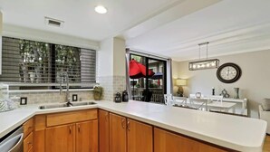 A modern kitchen with wooden cabinets, a white countertop, a sink, and a window with blinds. - Updated Beach Villa  2 bd 2 ba  just steps 2 sand! (Hilton Head Island)