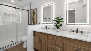 Un baño moderno con cabina de ducha de vidrio, inodoro blanco, armarios de madera y encimera de mármol.