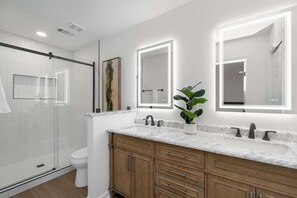 A modern bathroom with a glass shower enclosure, a white toilet, wooden cabinets, and a marble countertop.