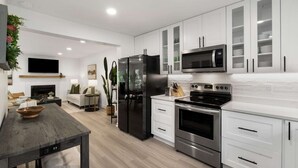 Una cocina moderna con armarios blancos, electrodomésticos de acero inoxidable y una zona de comedor con mesa de madera.