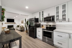 A modern kitchen with white cabinets, stainless steel appliances, and a dining area with a wooden table.