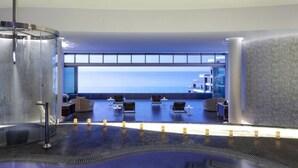 A modern indoor pool area with lounge chairs and a view of the sea.