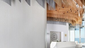 A modern lobby with a reception desk, seating area, and a view of the sea.