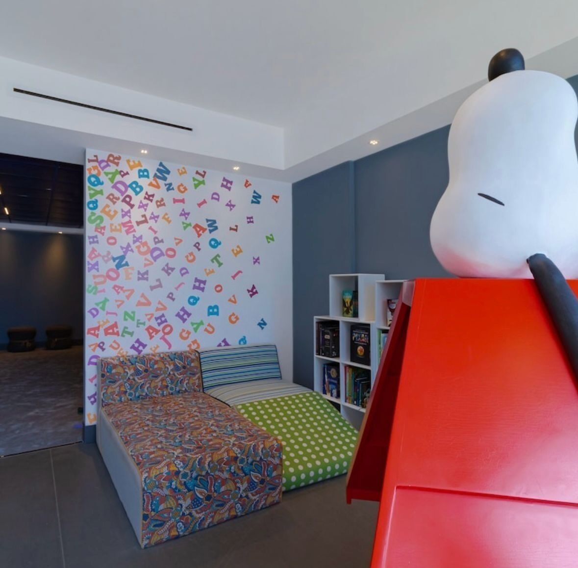 A modern room with a colorful alphabet wall, a sofa with patterned cushions, and a bookshelf.