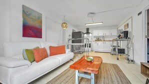 A modern living room with a white sofa, a wooden coffee table, and a kitchen area with white cabinets and a stainless steel refrigerator. - Cozy Beach Apartment (Aguadilla)