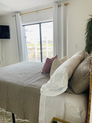 Relax in this serene bedroom with a large bed, sliding glass door to a deck, and a TV for entertainment.