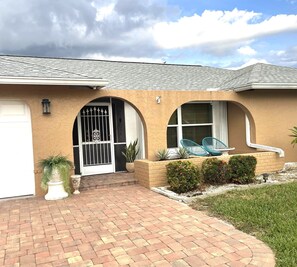 Stucco home with a garage and porch area, featuring large windows and a bird perched on the roof.