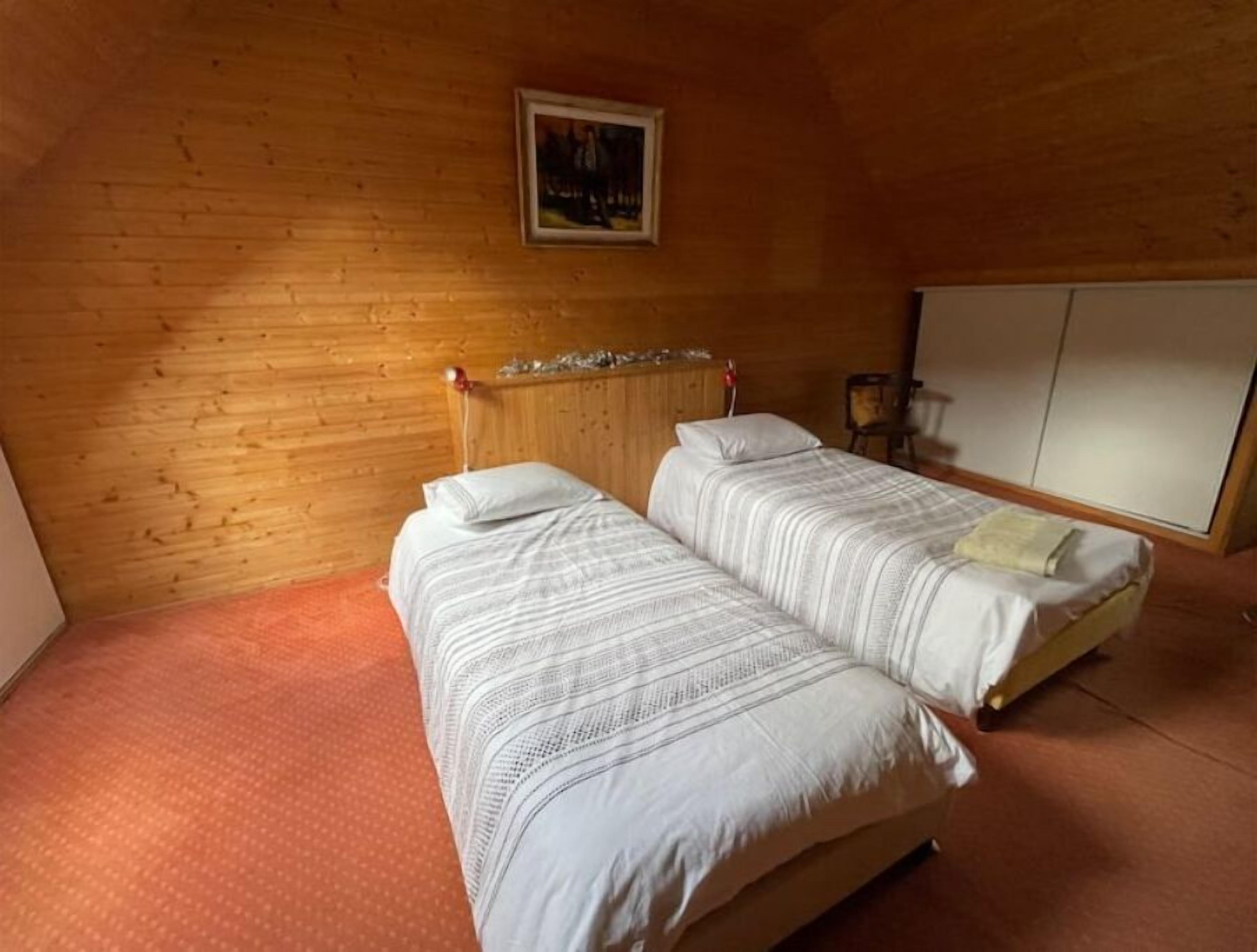 Quarto com duas camas, paredes de madeira, um quadro e um guarda-roupa.