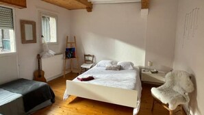Ein Schlafzimmer mit Holzboden, einem Bett, einem Stuhl, einer Gitarre und einer Leiter.