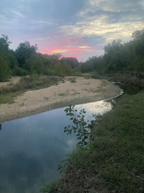 A river with a grassy bank and trees in the background. - Private Happy Camper on the Water - kayaks and lily pad available on property. (Hematite)