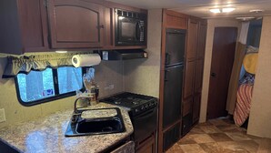 Cocina compacta con estufa, microondas y refrigerador, ventana con cortinas y piso de tablillas.