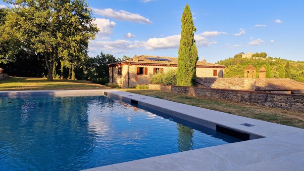 Une piscine avec une terrasse en pierre, un mur en pierre et, au fond, un bâtiment doté d’un toit en tuiles.