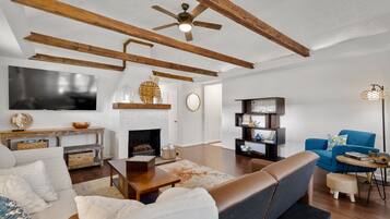 A living room with a fireplace, wooden beams, a blue sofa, and a television.