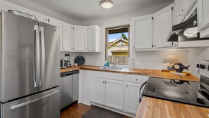 A modern kitchen with white cabinets, stainless steel appliances, and a wooden countertop.
