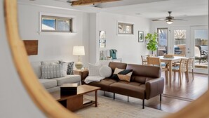 A living room with a brown sofa, a coffee table, and a dining area with wooden chairs and a table.