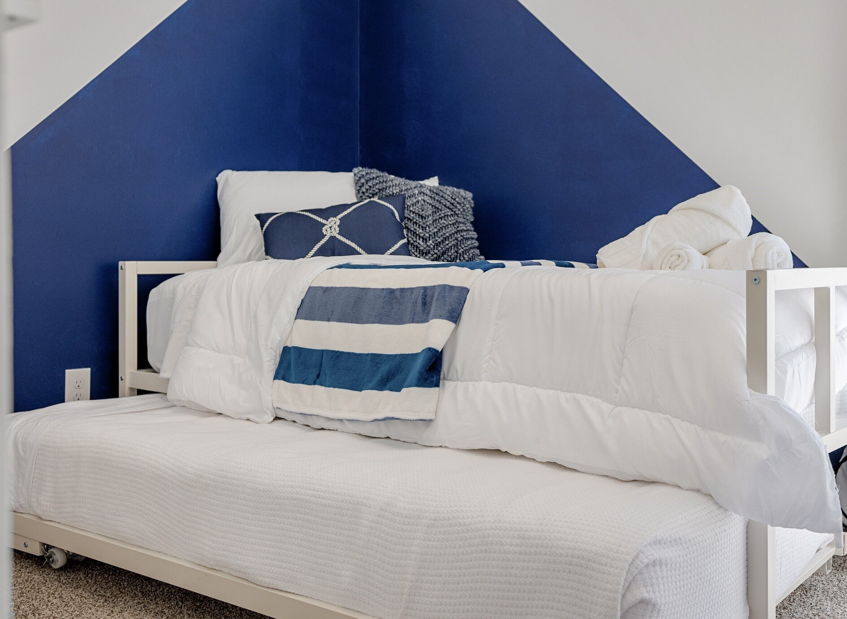A bed with white bedding and a blue and white striped blanket, set against a blue wall with a geometric design.