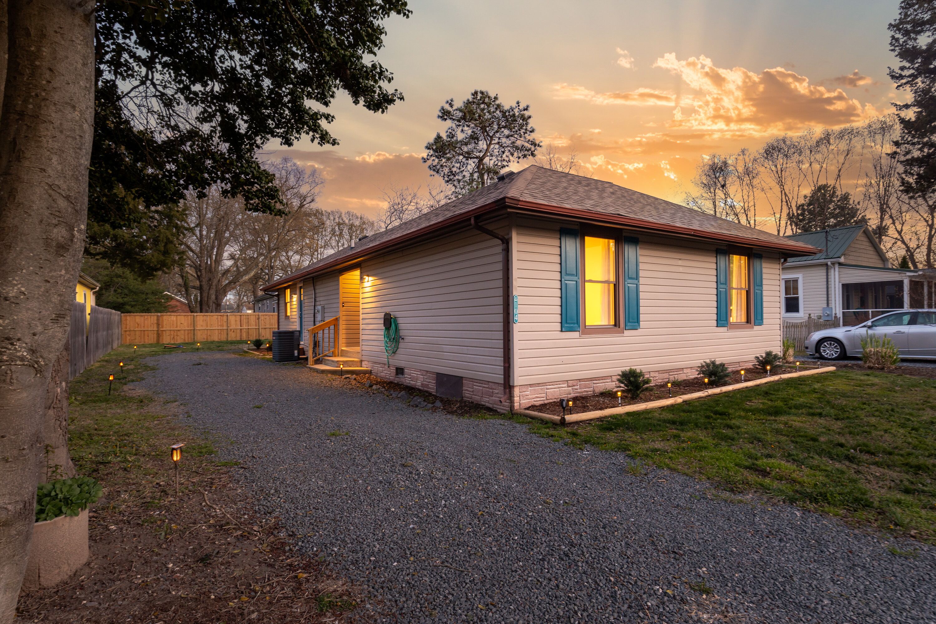 Une maison de plain-pied avec une allée gravillonnée, une clôture en bois et une voiture garée dans l’allée.