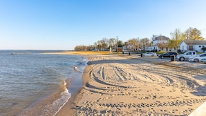 A beach with footprints leading to a parking area with cars.