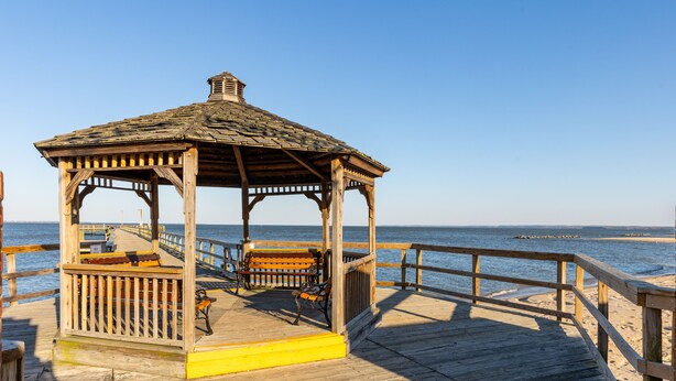 A wooden gazebo with benches, a yellow-painted floor, and a view of the ocean.