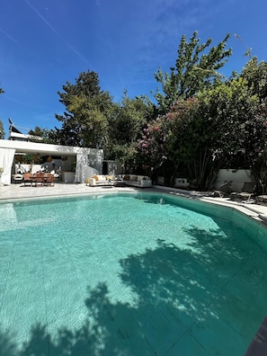 Una piscina azul cristalina con sillas de descanso y una zona de estar cubierta.