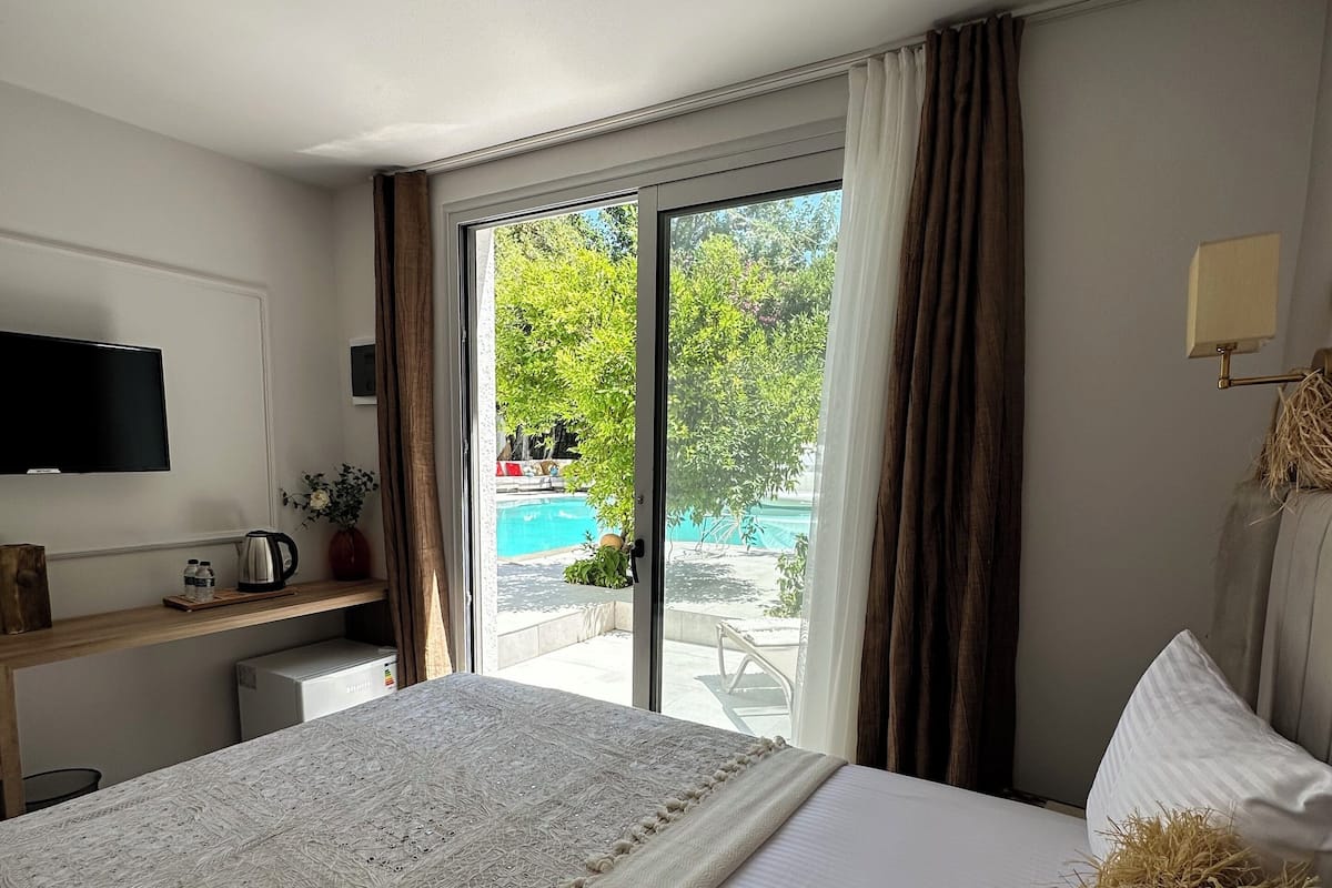 Habitación de hotel con una cama grande, televisión, escritorio con hervidor y vista a una piscina por una puerta de cristal.