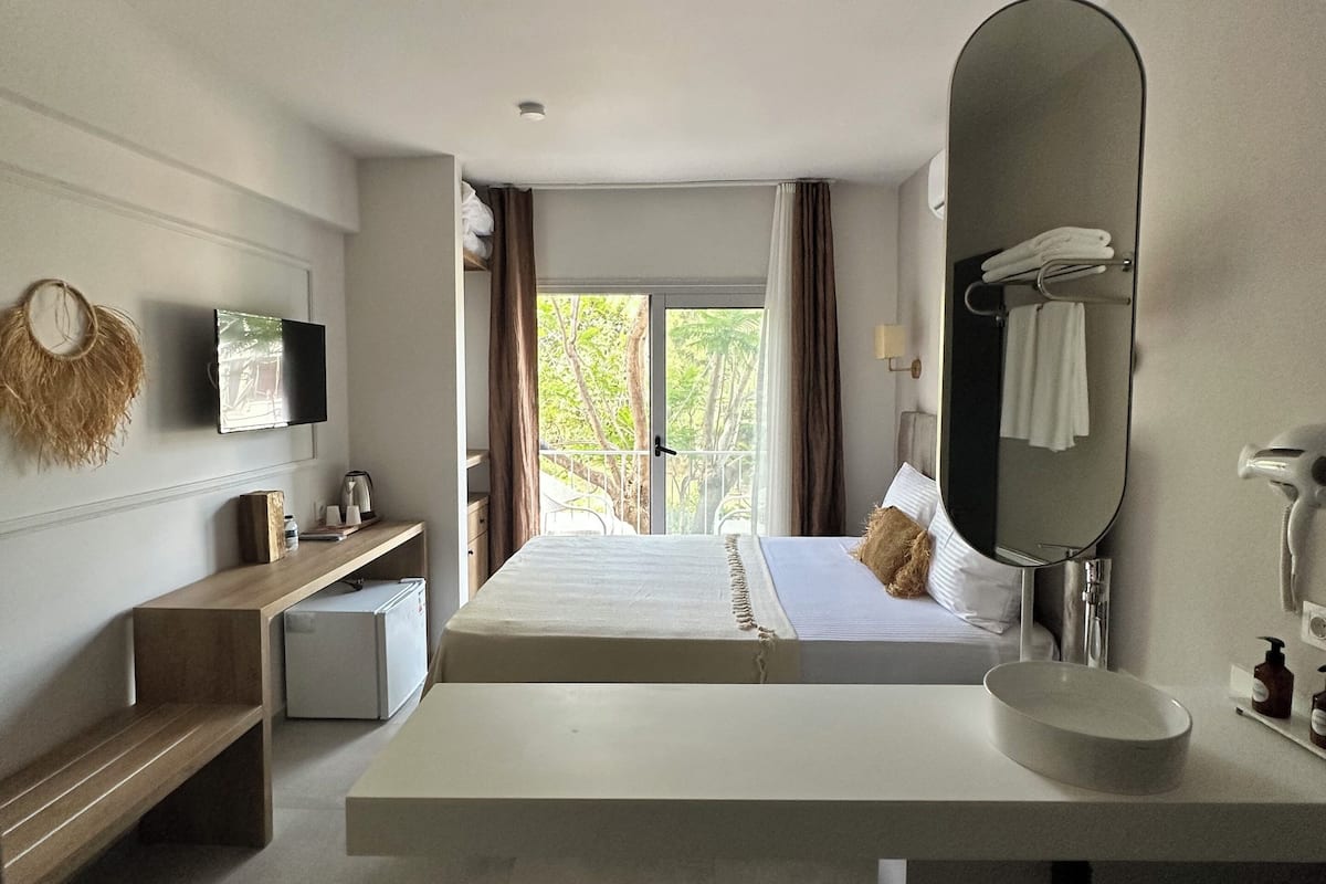 Una habitación de hotel moderna con una cama grande, un escritorio integrado, un televisor de pantalla plana, un espejo amplio y vistas al exterior.