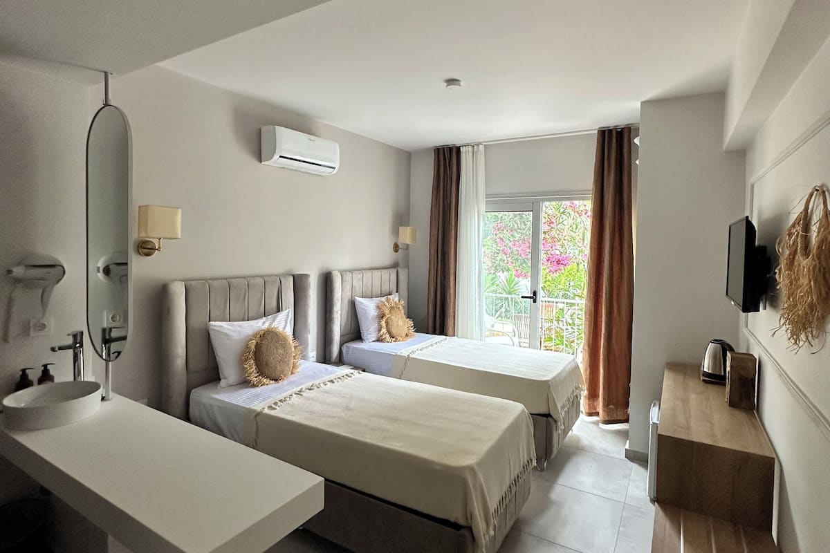Una habitación de hotel moderna con dos camas, un ventanal con cortinas, un televisor de pantalla plana y una mesita de madera con hervidor.