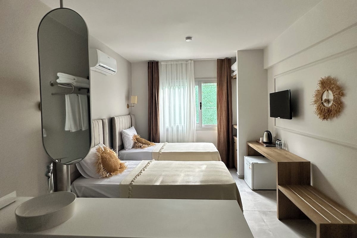 Habitación de hotel moderna con una cama grande, una mesita de noche, un espejo, un televisor y una pequeña kitchenette.